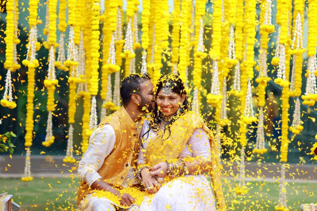 Joyful haldi flower shower moment where the groom kisses the smiling bride surrounded by yellow marigold decor, captured by Chikkarams Wedding Photography in Hyderabad